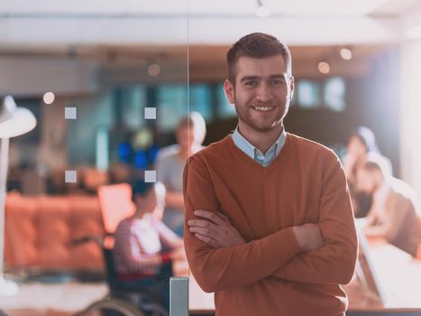 Handsome casual businessman standing confident in the office. Disabled businesswoman in wheelchair working together with the team in the background. High quality photo. Follow focus. 