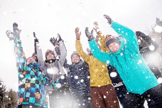 group of young happy business people having fun throwing snow in the air while enjoying snowy winter day with snowflakes around them during a team building in the mountain forest