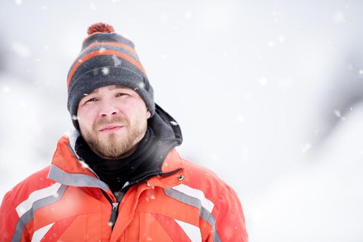 Man in winter season  Portrait of young man in warm clothes enjoying snowy day with snowflakes around him in the winter forest