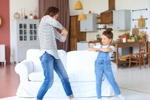 Cheerful mother with little daughter dancing at favourite song in living room at home