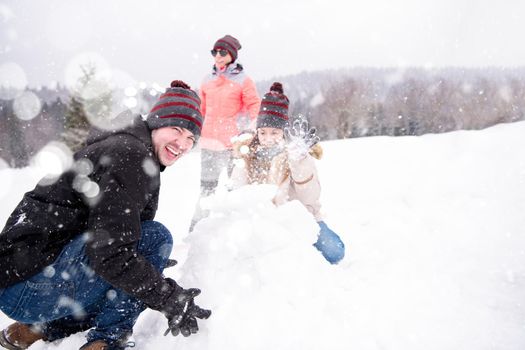 group of young happy business people having a competition in making snowmen while enjoying snowy winter day with snowflakes around them during a team building in the mountain forest