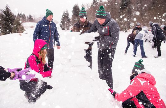 group of young happy business people having a competition in making snowmen while enjoying snowy winter day with snowflakes around them during a team building in the mountain forest