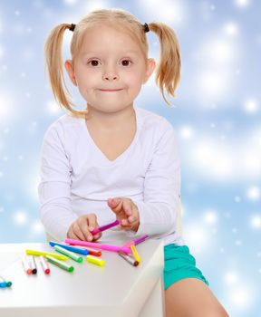 Pretty little blonde girl drawing with markers at the table.Girl holding in hands a pink marker.The concept of celebrating the New year, Holy Christmas, or child's birthday on a blue