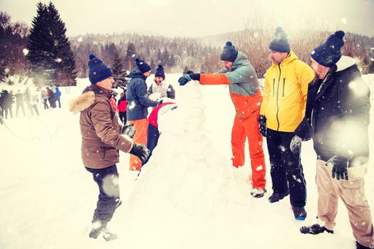 group of young happy business people having a competition in making snowmen while enjoying snowy winter day with snowflakes around them during a team building in the mountain forest
