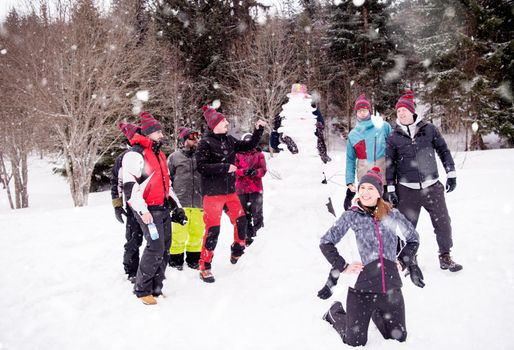 group portrait of young happy business people after a competition posing with finished snowman while enjoying snowy winter day with snowflakes around them during a team building in the mountain forest