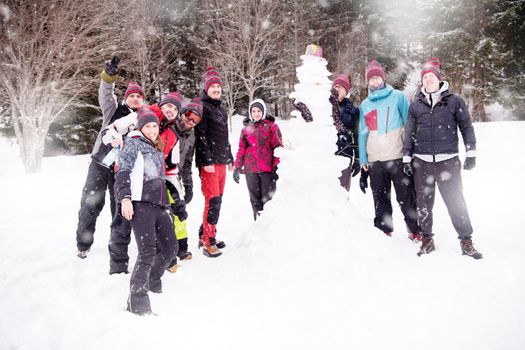 group portrait of young happy business people after a competition posing with finished snowman while enjoying snowy winter day with snowflakes around them during a team building in the mountain forest