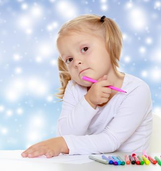 Pretty little blonde girl drawing with markers at the table.The girl thoughtfully looks into the camera.The concept of celebrating the New year, Holy Christmas, or child's birthday on a blue
