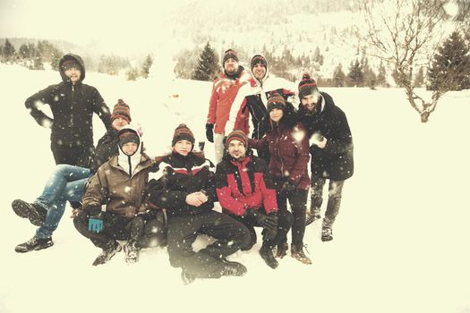 group portrait of young happy business people after a competition posing with finished snowman while enjoying snowy winter day with snowflakes around them during a team building in the mountain forest