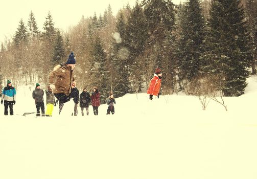 group of young happy business people having a running in bag competition while enjoying snowy winter day with snowflakes around them during a team building in the mountain forest