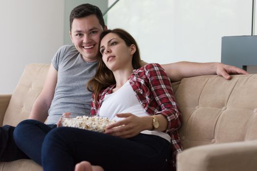 young handsome couple enjoying free time watching television with popcorn in their luxury home villa