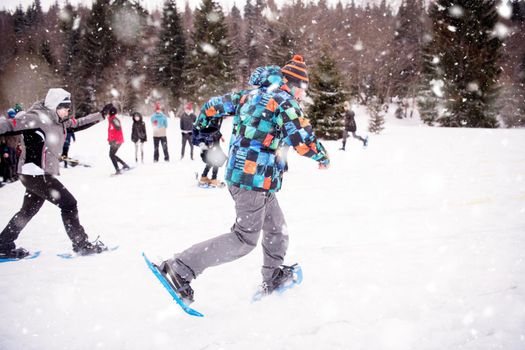 group of young happy business people having a running competition using snowshoes while enjoying snowy winter day with snowflakes around them during a team building in the mountain forest