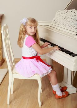 Cute little blonde girl plays the piano facing away from the tool