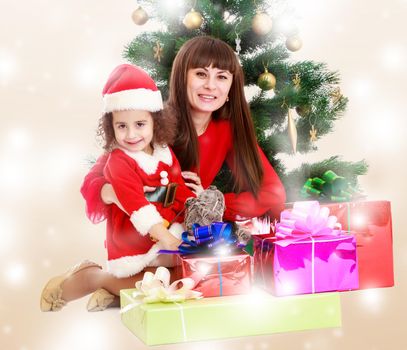 Happy mother and daughter near a Christmas tree surrounded by heaps of gifts.Winter brown abstract background with white snowflakes.