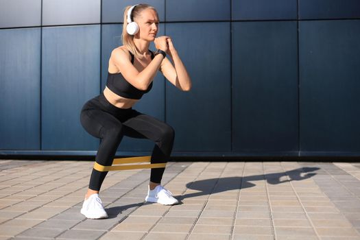 Sporty woman doing squats with fitness gum expander outdoors