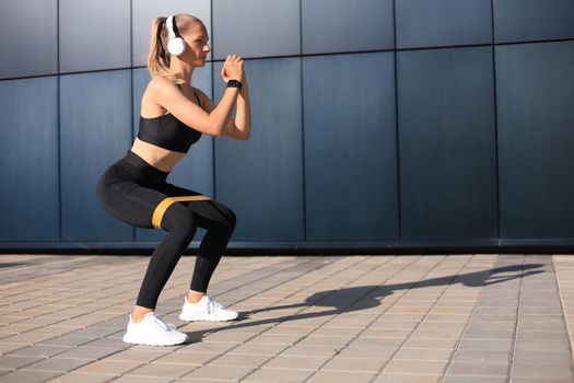 Sporty woman doing squats with fitness gum expander outdoors