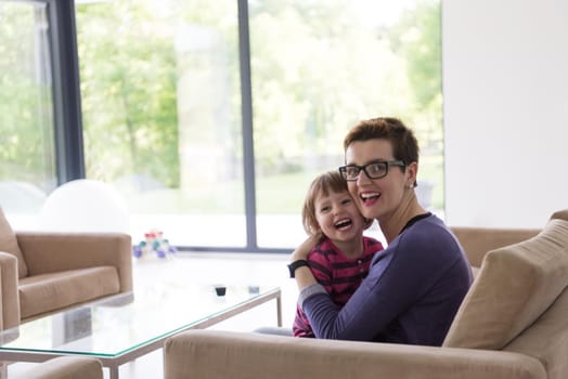 young mother and cute little girl enjoying their free time hugging on the sofa in their luxury home villa