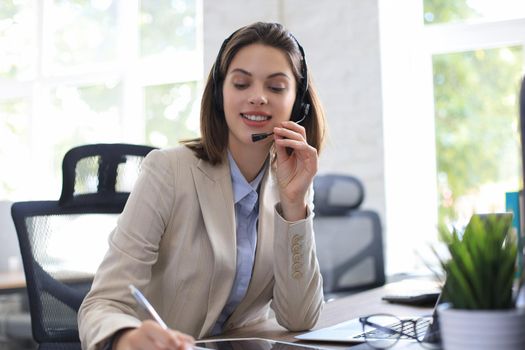 Cheerful female manager sitting at office desk and performing corporate tasks using wireless connection on digital gadgets