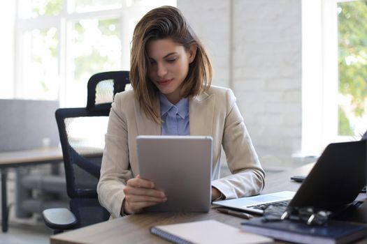 Attractive smiling woman working on a tablet in modern office