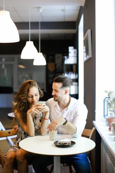 Young pretty husband hugging wife and sitting at cafe, drinking coffee. Concept of enjoing togetherness and having lunch.