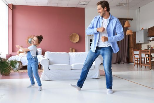 Handsome young man dancing at home with his little cute daugther