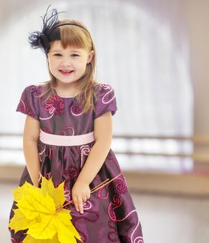 In a room with a large semi-circular window. Nice little girl dressed in brown dress. She is holding a bouquet of maple leaves.