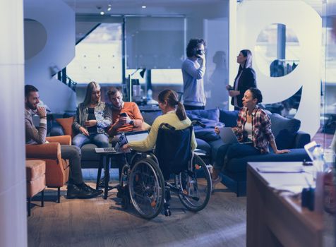 Handicapped businesswoman in a wheelchair on meeting with her diverse business team brainstorming about ideas and plans in a modern open space coworking office space. High quality photo