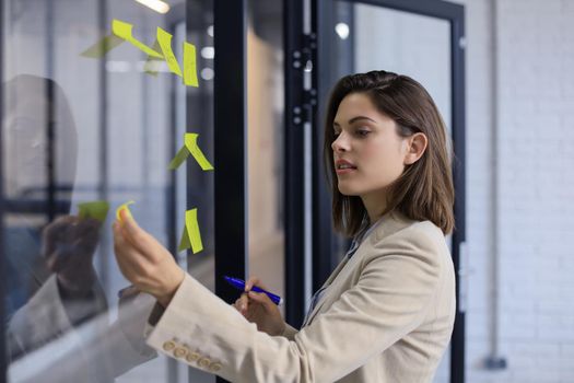 Attractive business woman post stickers on glass at office and writing on them