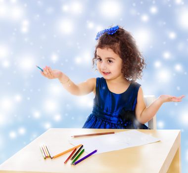 Adorable little girl in a blue dress drawing pencils . Girl sitting at the table.Blue winter background with white snowflakes.