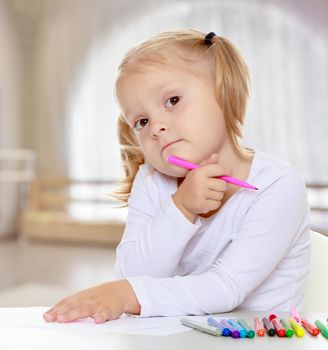Pretty little blonde girl drawing with markers at the table.The girl thoughtfully looks into the camera.The concept of pre-school education of the child among their peers . in gaming room