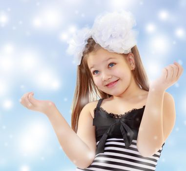 Beautiful, chubby, long-haired little girl with big white bows on the head . girl gesturing with his hands. Close-up.Blue Christmas background with white snowflakes.