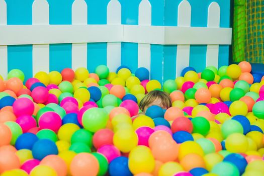 Happy little kid boy playing at colorful plastic balls playground high view. Funny child having fun indoors.