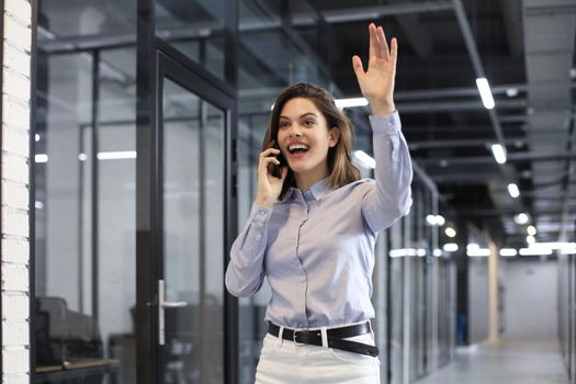 Attractive business woman talking by smartphone and waving hand by greeting you