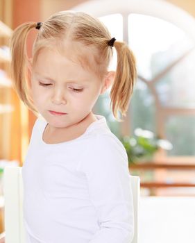 The concept of pre-school education of the child among their peers . in gaming room with a large arched window.Distressed small, blonde girl with white t-shirts without a pattern.