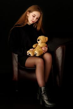 Beautiful teenage girl with a teddy bear on a black background. Concept layout for magazine cover.