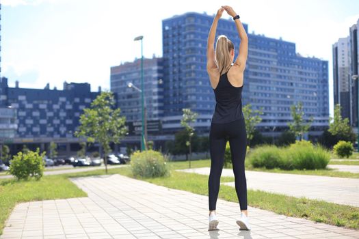 Back view of young fitness woman wearing sports clothing exercising outdoors, stretching exercises
