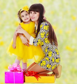 Beautiful young mother and her cute little daughter , embracing, surrounded by Christmas gifts.Bright,floral yellow-green blurred background.