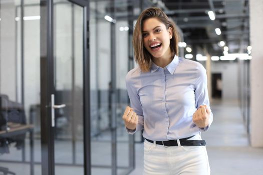 Beautiful businesswoman is keeping arms raised and expressing joyful in office