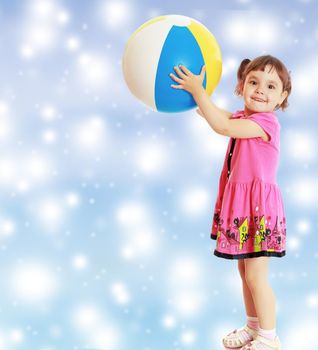 Happy little girl with pigtails on the head , in a pink dress. The girl lifted a large, inflatable striped ball.On new year or Christmas blue background with white big stars.
