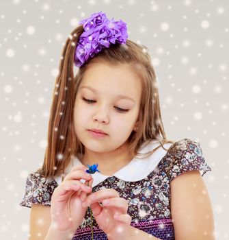 Sad little girl with a big purple bow on her head looks at little flower. It's about something thought. Close-up.On the Christmas background with white snowflakes.
