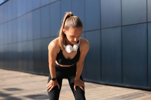 Young fitness attractive sporty girl resting after intensive evening run outdoor at sunset in city