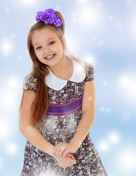 Happy long-haired little girl with a big purple bow on her head , and fancy dress. Close-up.Blue Christmas background with white snowflakes.