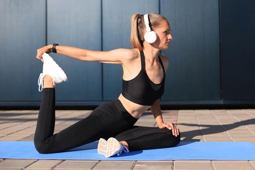 Attractive young fitness woman wearing sports clothing exercising outdoors, stretching exercises