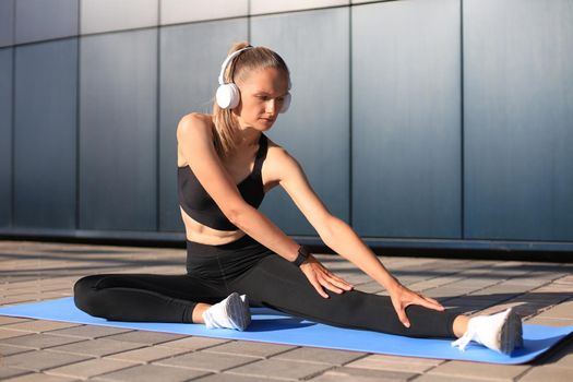 Attractive young fitness woman wearing sports clothing exercising outdoors, stretching exercises