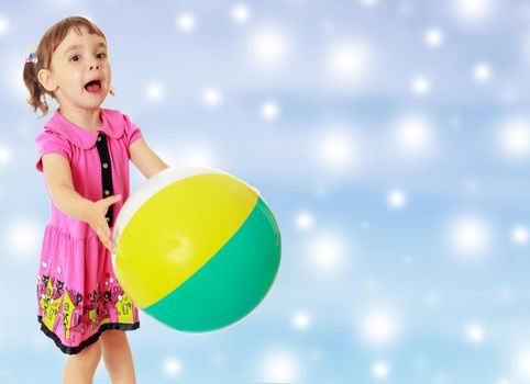 Emotional little girl with pigtails on the head , in a pink dress. Girl catches with hands a large, inflatable striped ball.On new year or Christmas blue background with white big stars.