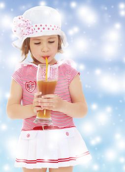 Cute little girl in pink sea dress and white hat with a large bow. Girl drinking through a straw apple juice from a large glass.Gentle blue Christmas background with white snowflakes abstract.
