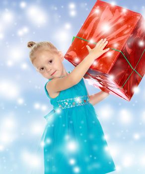 Caucasian little girl in a blue dress, holding the hands of the big red box that is a gift.The girl lifted the box over his head.The concept of celebrating the New year, Holy Christmas