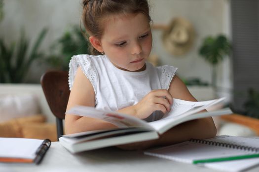 Little girl sits at the desl at home and does homework, self study of the material, reading book. The concept of distance education