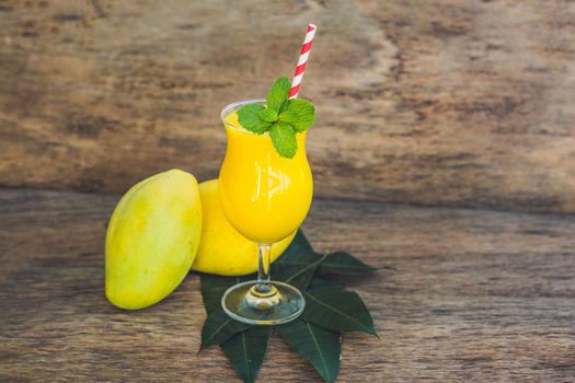 Juicy smoothie from mango in glass with striped red straw and with a mint leaf on old wooden background. Healthy life concept, copy space.