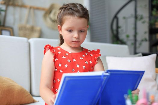 Little girl sits at the desl at home and does homework, self study of the material, reading book. The concept of distance education