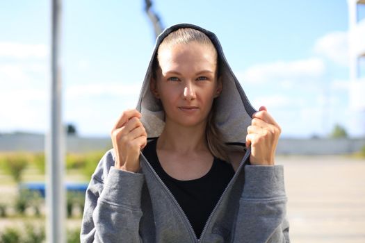 Concentrated athletic caucasian woman with a hood on her head wearing gray hoodie looking to the camera